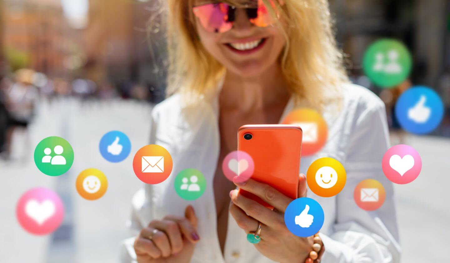 Woman looks at phone with social media icons floating around her.