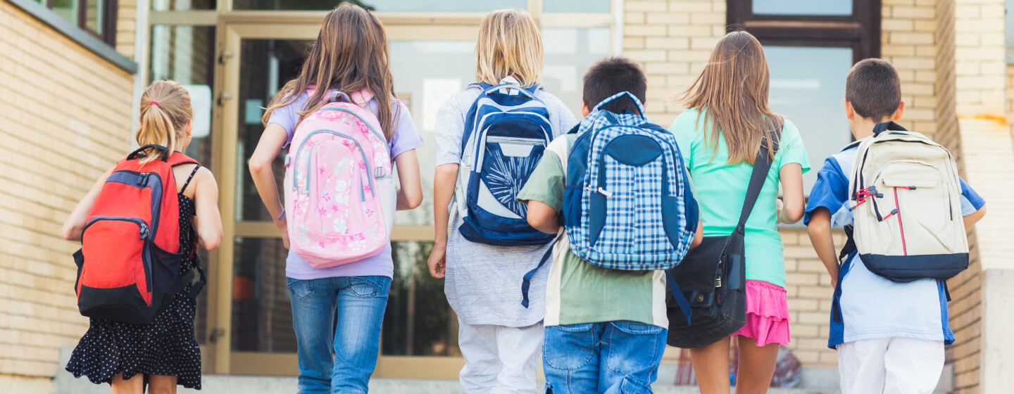 School children with backpacks walk into school building.