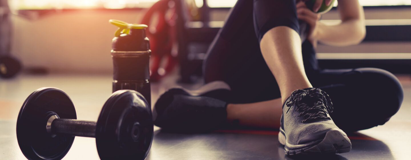 Woman sitting on gym floor next to dumbbell and water bottle.