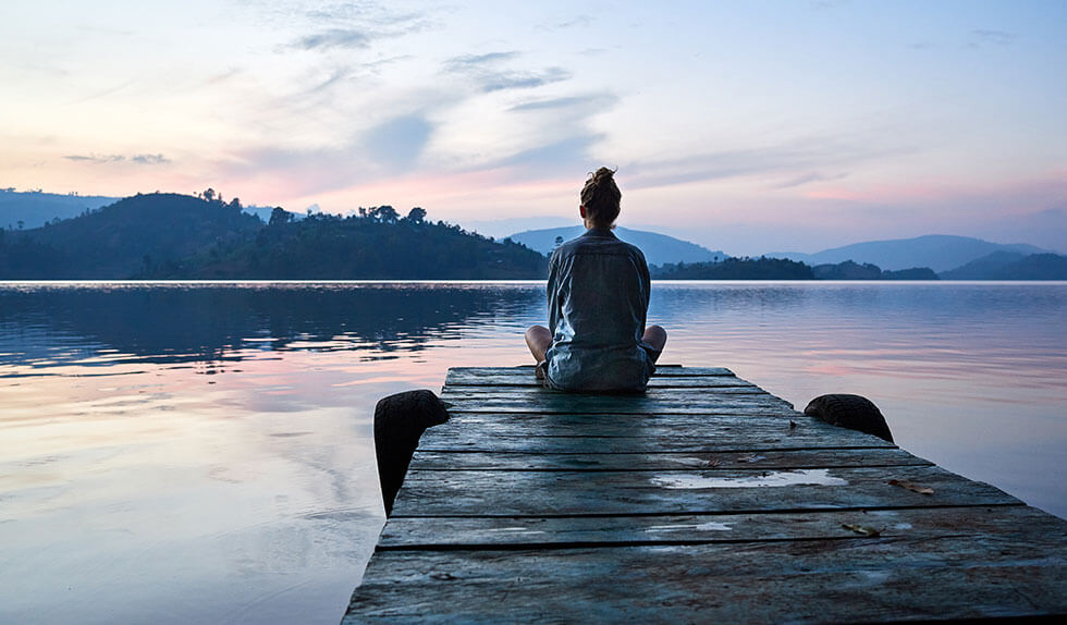 Woman meditates on beautiful lake dock.