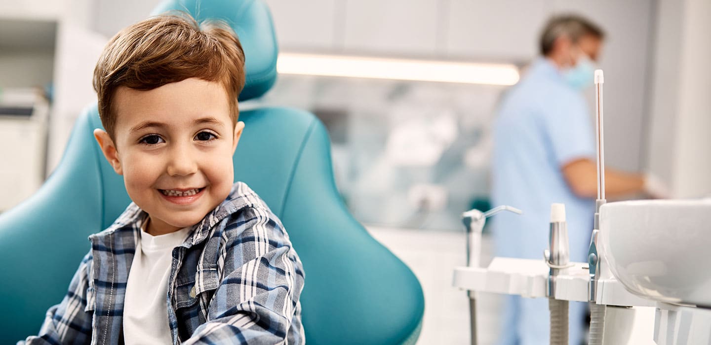 Cute kid in dental chair with dental clinic owner in the background