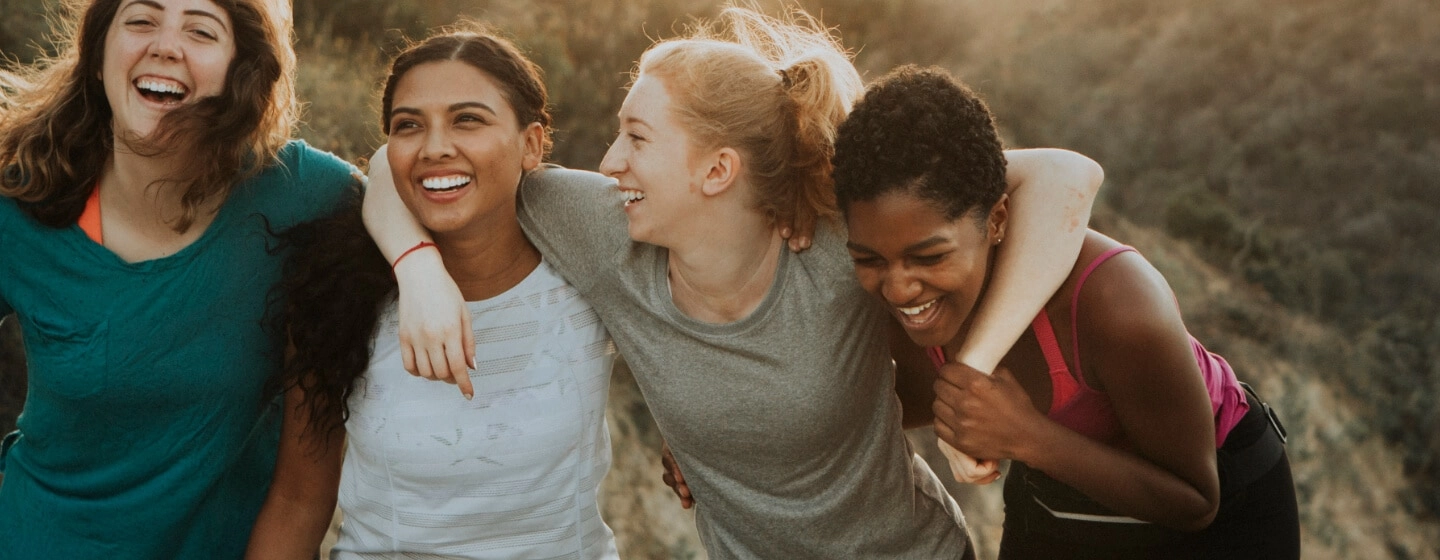 A group of women laughing with arms around each other's shoulders