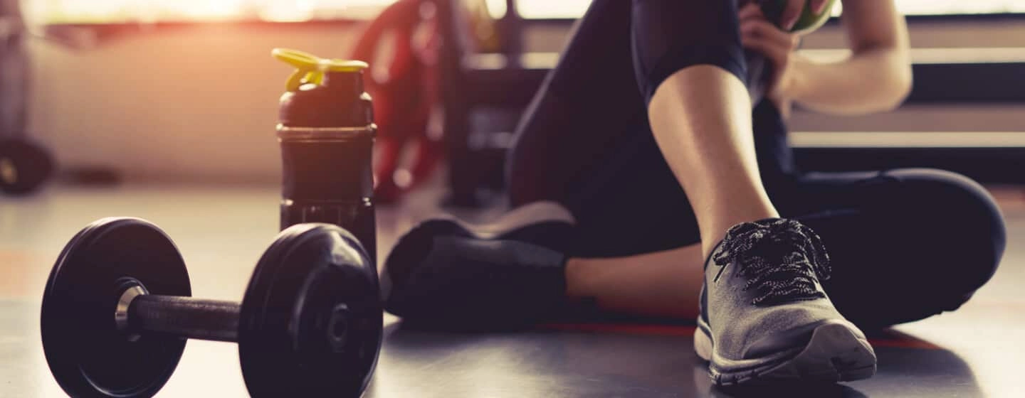 Woman sitting on gym floor next to dumbbell and water bottle