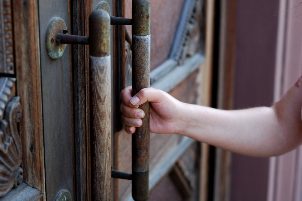 A hand pulling open a heavy wooden door, representing a behavioral health practice answering a prospective patient's first contact.