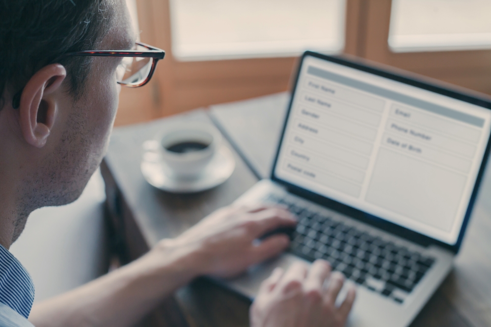 Man in glasses filling out an online contact form on a laptop, with a cup of coffee on the table beside him