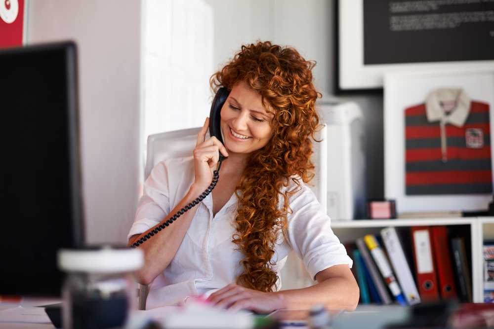 Intake coordinator at a behavioral health practice smiling as she answers a prospective patient's call at her desk.